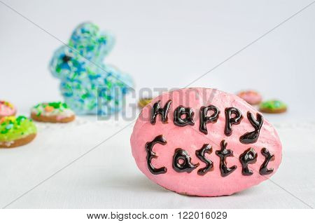 Pink Easter homemade gingerbread cookie in form of egg with words Happy Easter on background of Easter rabbit and eggs. Delicious Easter cookies background. Selective focus.