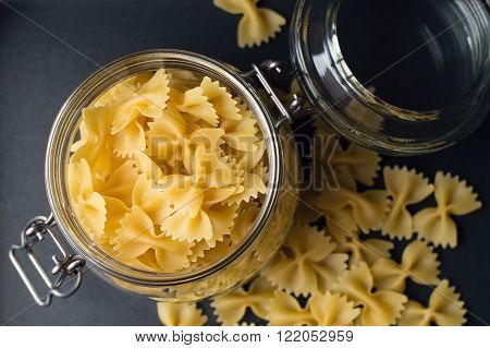 Uncooked italian pasta stored in a glass container dark background