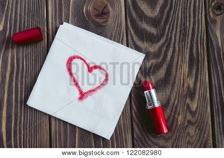 Note on the napkin red heart red lipstick on a dark brown wooden background.