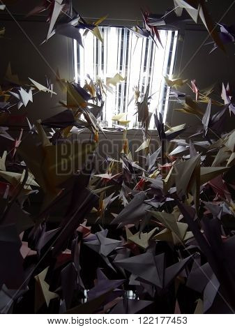 Handmade colored origami cranes on ceiling strings under light lamp