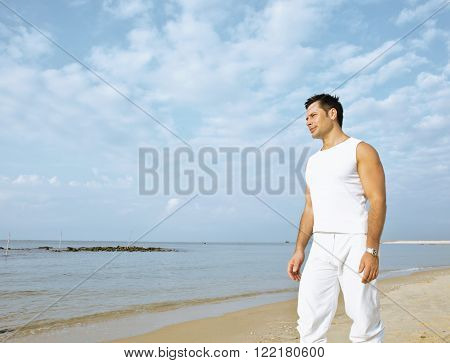 young brunette man on beach at sea smiling, gomosexual in white dress big muscles