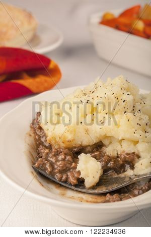 Homemade partially-eaten shepherd's pie dinner with bread and roasted vegetables in the background.