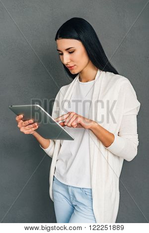 Enjoying her new touchpad. Beautiful young woman using her digital tablet while standing against grey background