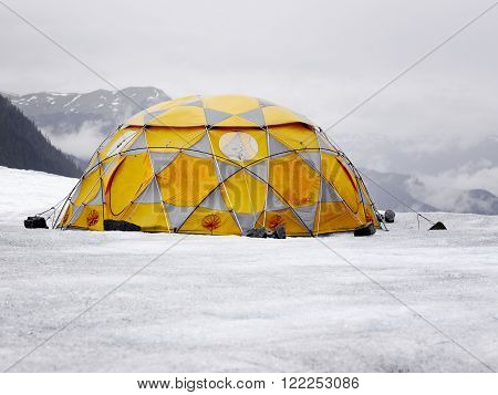 Camping in the high mountains. Orange and grey tent on the glacier.