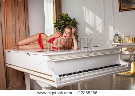studio glamour photo of female model lying in red lingerie on piano