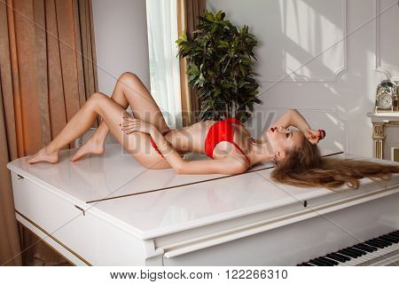 studio glamour photo of female model lying in red lingerie on piano