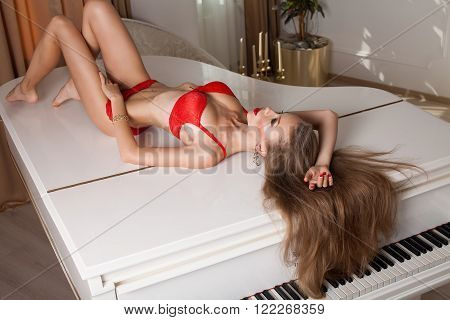 studio glamour photo of female model lying in red lingerie on piano