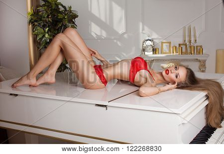 studio glamour photo of female model lying in red lingerie on piano