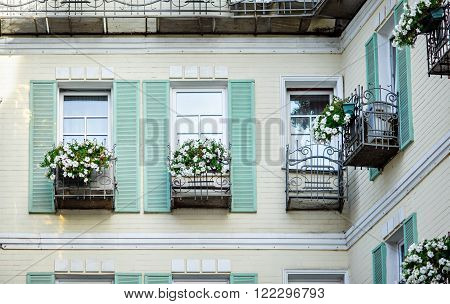 Typical facade of the old Provencal retro house with windows and wooden shutters decorated with colorful fresh flowers