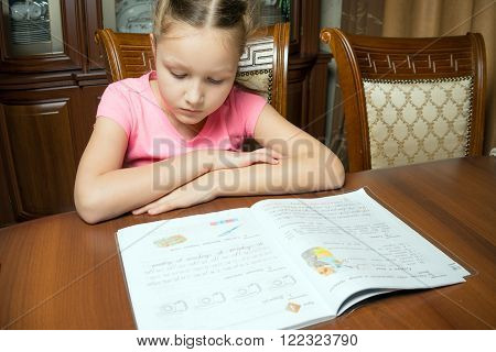 Girl doing homework. She writes in a notebook at the table.