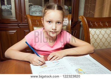 Girl doing homework. She writes in a notebook at the table.