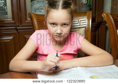 Girl doing homework. She writes in a notebook at the table.