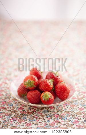 Small group of fresh strawberries on a small antique bone china plate. plate is on pretty floral fabric.