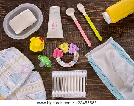 Japanese diapers wet wipes soap baby powder cream tither cotton buds spoons soother and duckling on dark brown wooden background. Flat lay or top view
