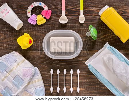Japanese diapers wet wipes soap baby powder cream tither cotton buds spoons soother and duckling on dark brown wooden background. Flat lay or top view