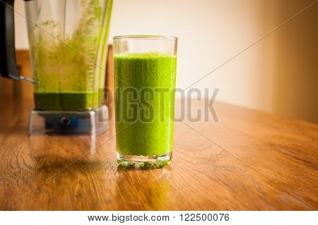 Vibrant healthy green smoothie with a blender in the background on a wooden table