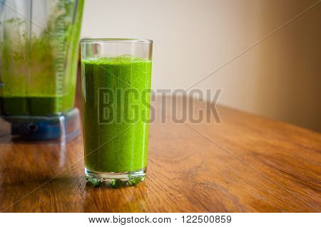 Vibrant healthy green smoothie with a blender in the background on a wooden table
