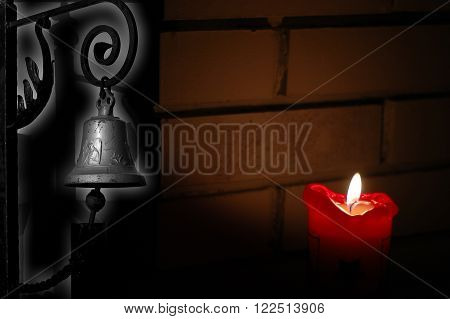 Picture shows old rustic light with a churchbell around the corner with a shadow from a candle light. Background is a brick wall.