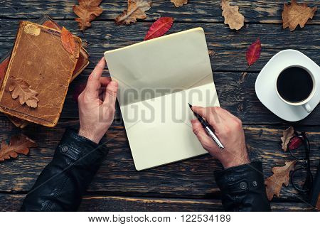 Male writes in a notebook sitting at a wooden table in the park. top view