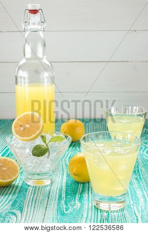 lemonade or limoncello in glasses with ice cubes sherbet glass with ice cubes decorated by mint leaf lemon fruits on turquoise colored wooden table