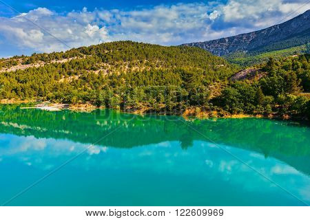 Mountain canyon Verdon in the French Alps. Smooth emerald green water of Lake Sainte-Croix-du-Verdon reflects the sky and wooded shore