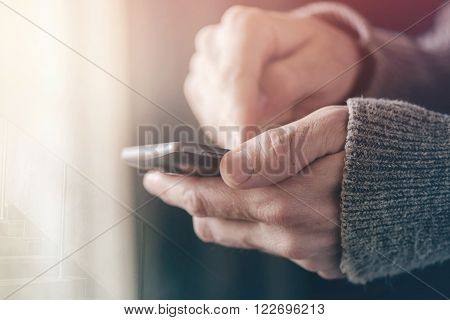 Casual man texting message on smartphone morning sunlight through window male hands using mobile phone device selective focus with shallow depth of field.
** Note: Shallow depth of field