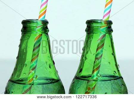 Close up view of two Glass Bottle of Water Necks with color striped straws at sunny summer day.