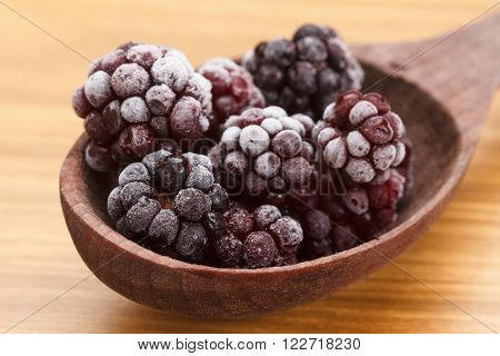 Macro view on frozen Blackberry fruits in spoon wooden background