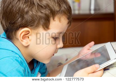 Boy with tablet lies in bed. Portrait of a child.
