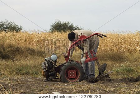 DIKANKA UKRAINE - SEPTEMBER 30 2015: Country farmer is plowing his garden with walk-behind garden tractor against the backdrop of a corn field
