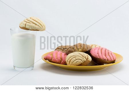A glass of milk next to a plate of concha bread