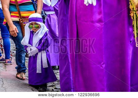 Antigua Guatemala - March 20 2016: Little boy wearing sunglasses & purple cucurucho outfit worn by penitent float bearers in Palm Sunday procession in colonial town with most famous Holy Week celebrations in Latin America.