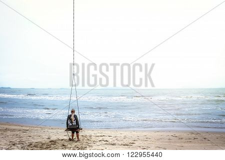 Single woman alone swinging and  looking into the distance over the horizon on a tropical beach with copy space. A bright sunlight illuminates the sea and the sky
** Note: Soft Focus at 100%, best at smaller sizes
