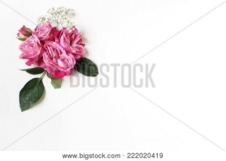 Decorative floral composition with pink roses, green leaves and and baby's breath Gypsophila flowers on white table background. Flat lay, top view, wedding or birthday styled stock photo.