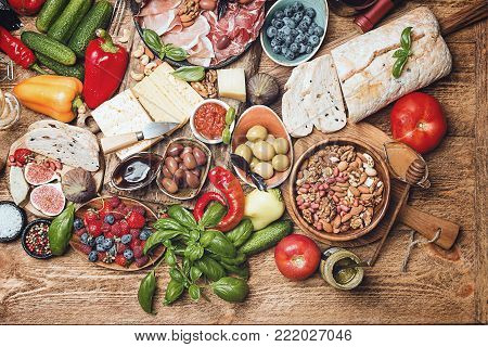 Top view table full of food. Italian antipasti wine snacks set. Cheese variety, nuts, Mediterranean olives, sauces, Prosciutto di Parma or jamon, tomatoes, vegatables and berries and wine over wooden background