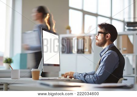 Young serious man with beard looking at computer monitor while concentratin on work