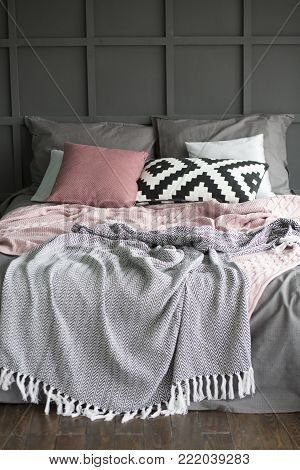a bed in an interior with pillows and plaids near a wall with geometry