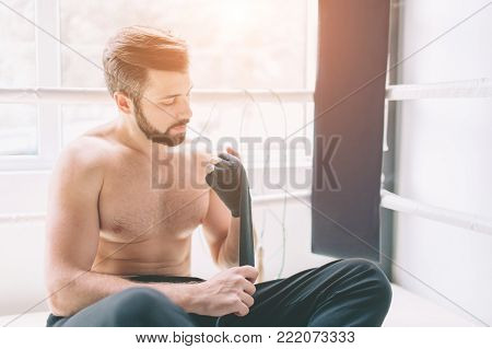 Handsome bearded boxer with bare torso wrapping his hands, ready to fight at the fight club
