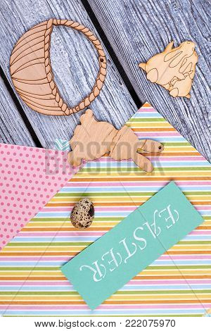 Easter card, wooden figurines, top view. Quail egg on colorful patterned sheets of paper, plywood rabbits and basket cutouts. Easter handmade decoration ideas.