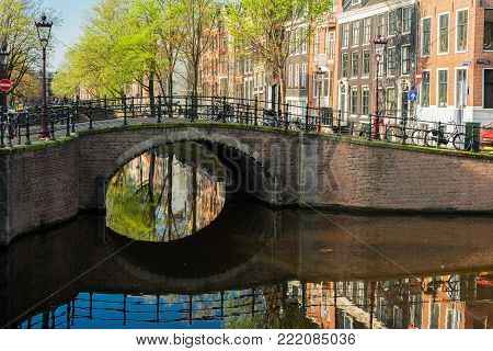 View of historical bridge over canal with mirror reflections in water at spring, Amstardam, Netherlands