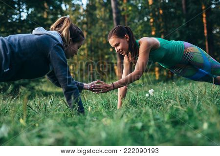 Two girls doing buddy workout outdoors performing push-ups to clap on grass.