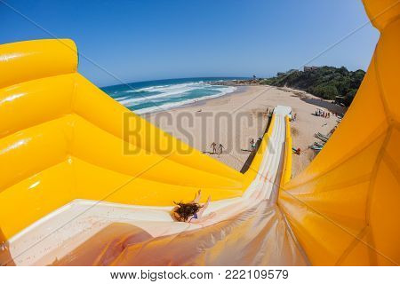 Beach Girl action thrill jump ride down high inflatable water slide summer holidays landscape.