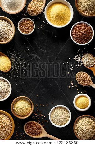 Various groats, cereals. Different types of groats in bowls and on a spoons on a  black background, top view. Healthy nutrition food