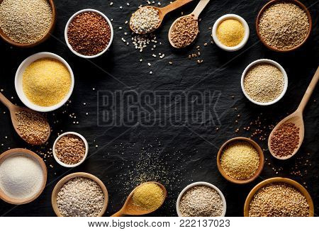 Various groats, cereals. Different types of groats in bowls and on a spoons on a  black background, top view. Healthy nutrition food