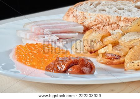 Tasty hazardous food. Greasy fried potatoes, bacon, red caviar, spicy sauce and white bread on a white plate. Russian snacking.
