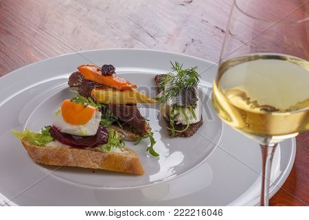 Glass of white wine and tartines with meat and veggies.