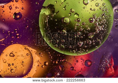 Unusual colorful background with oil drop circles and air bubbles that reflect yellow, orange, purple, green and red colors. Color spots intentionally unfocused. Cosmic space and galaxy concept.