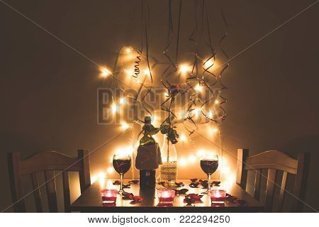 Home style restaurant interior at night. Table close up with glass of wine, lights and roses
