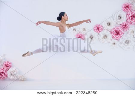 Young and incredibly beautiful ballerina is posing and dancing in a white studio full of light. The photo greatly reflects the incomparable beauty of a classical ballet art.