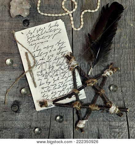 Paper manuscript with hand written text, pentagram and quill on planks. Occult, esoteric, divination and wicca concept. No foreign text, all symbols on pages are fantasy, imaginary ones